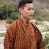 A Bhutanese man in traditional attire stands outdoors near Thimphu's serene countryside.